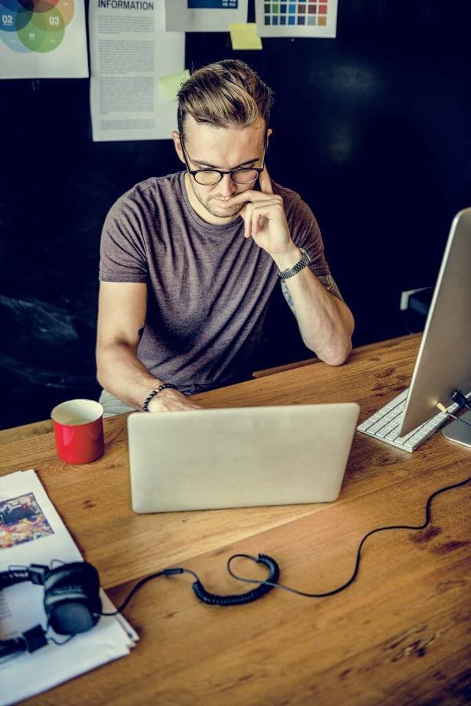 a bespectacled man studying his laptop screen